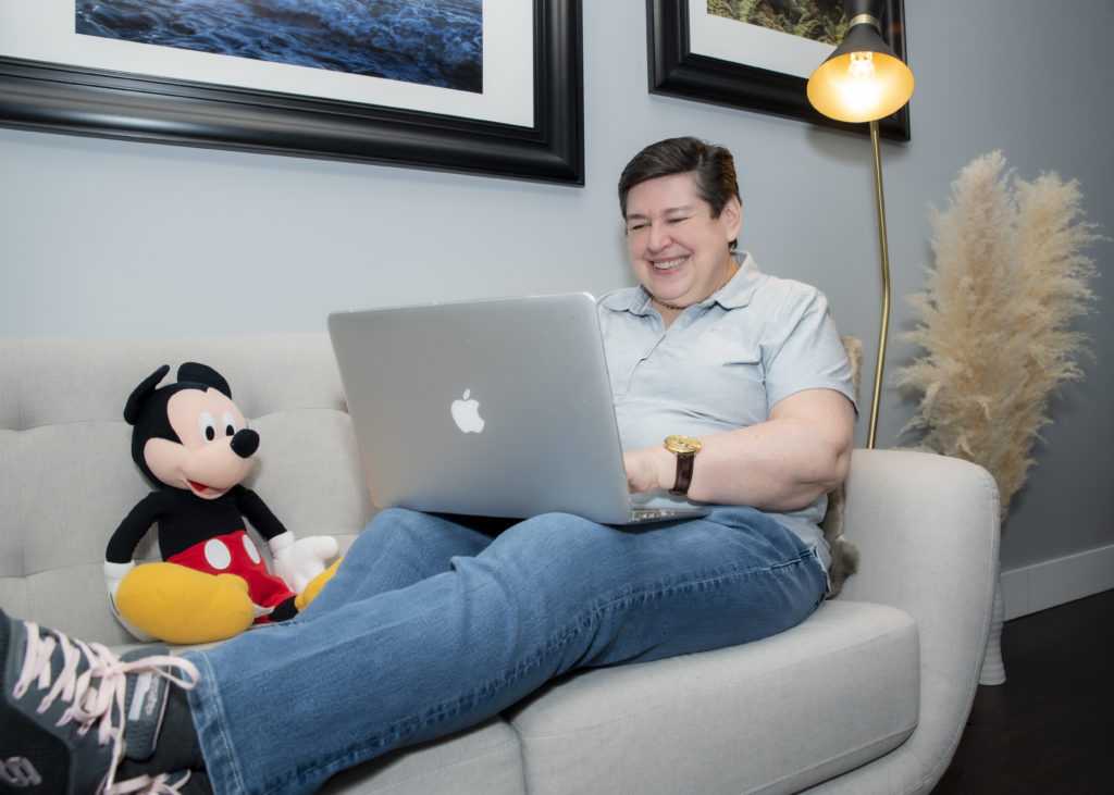 Real estate agent Darlene Smith sitting next to a Mickey Mouse plush toy on a sofa with a laptop hard at work