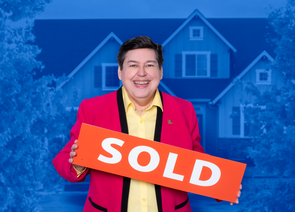 Photo of NB realtor Darlene Smith holding a sold sign in front of a family home that is tinted blue